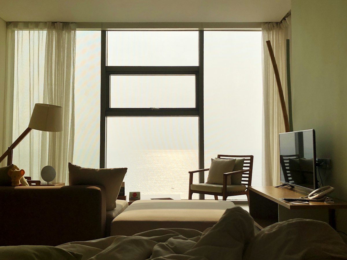 Soft-lit room with linen curtains and a wide window over a hazy sea